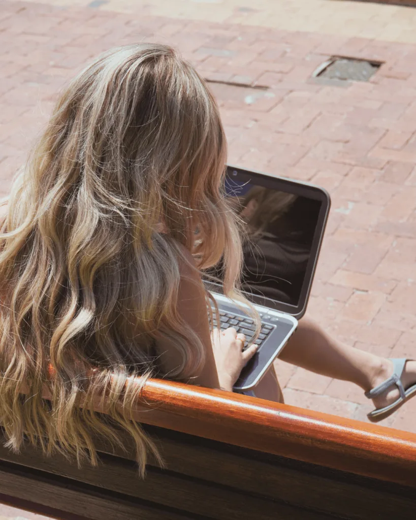 Woman on a bench working on a laptop.